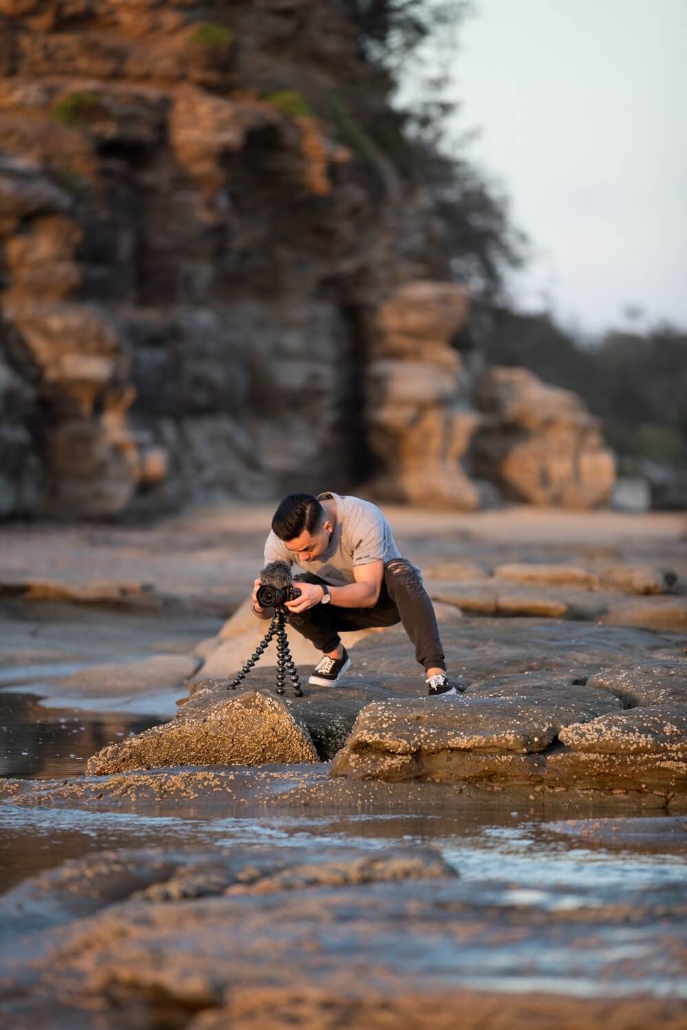 Man by the shore, taking photo of the sunset while using a tripod