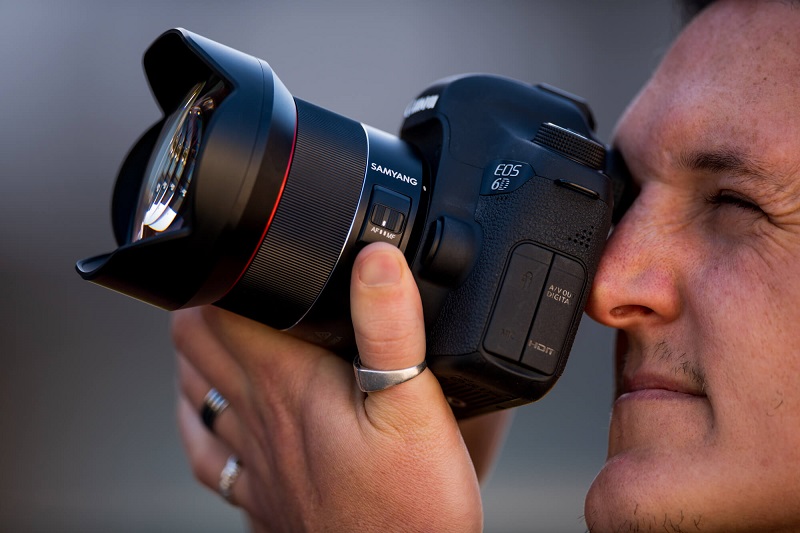 man looking at the viewfinder of a dslr camera