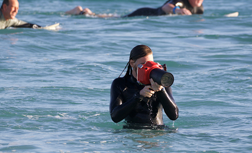 photographer in wet suit, taking pictures while on the beach