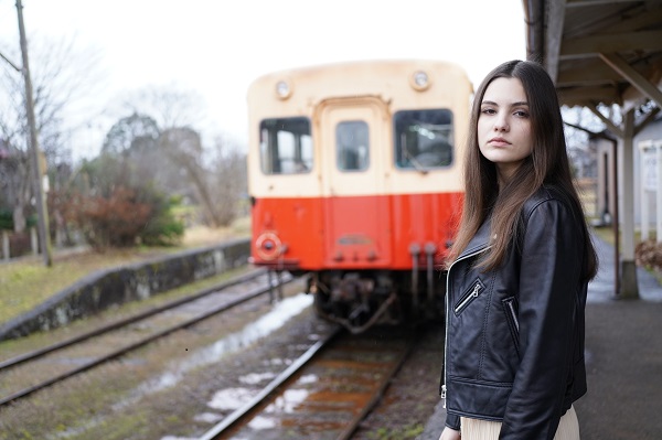 Young woman in a leather jacket standing on a train platform, photographed with the Sony 40mm f2.5 G lens