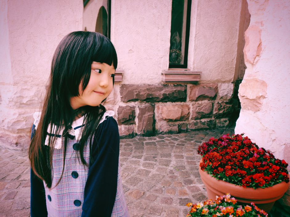 Girl in a tartan dress in front of a whitewashed stone building and flower pots, photographed with the Olympus EM10 Mark IV