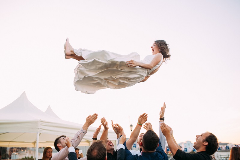 a candid wedding photo of the bride tossed up by a group of guys