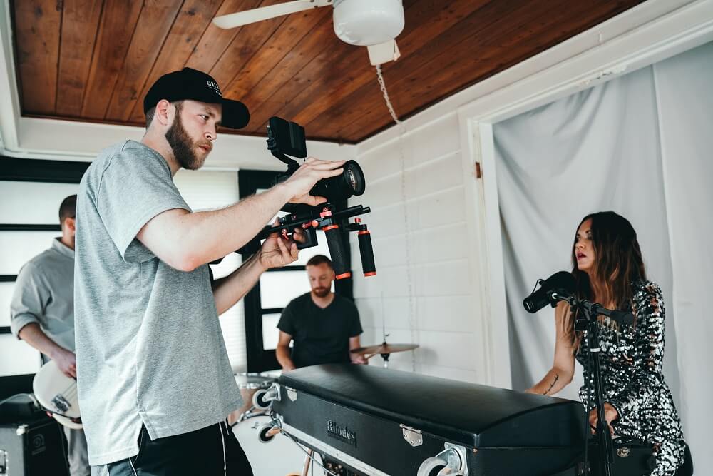 A group of people taking a video of a woman playing the piano