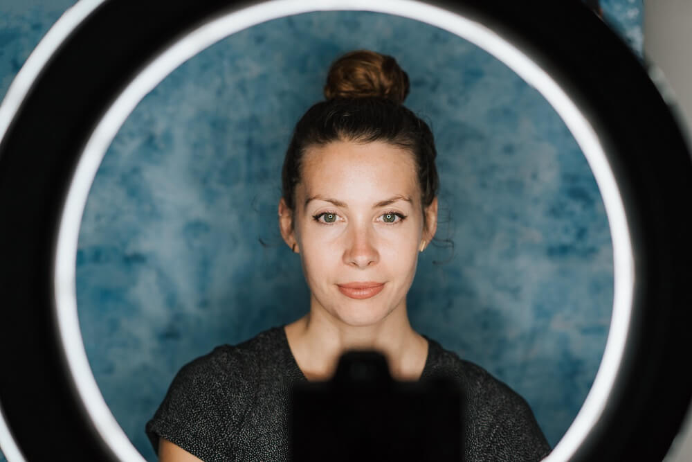 A woman in front of a camera, with a ring light